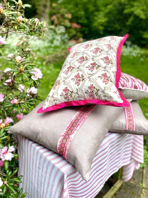 A pink floral cushion on top of glazed linen cushions in an outdoor setting.