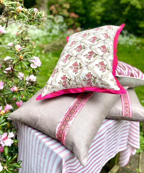 A pink floral cushion on top of glazed linen cushions in an outdoor setting.