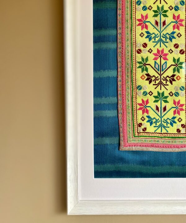 Bright acid yellow embroidery art textile framed in a white frame against teal silk.