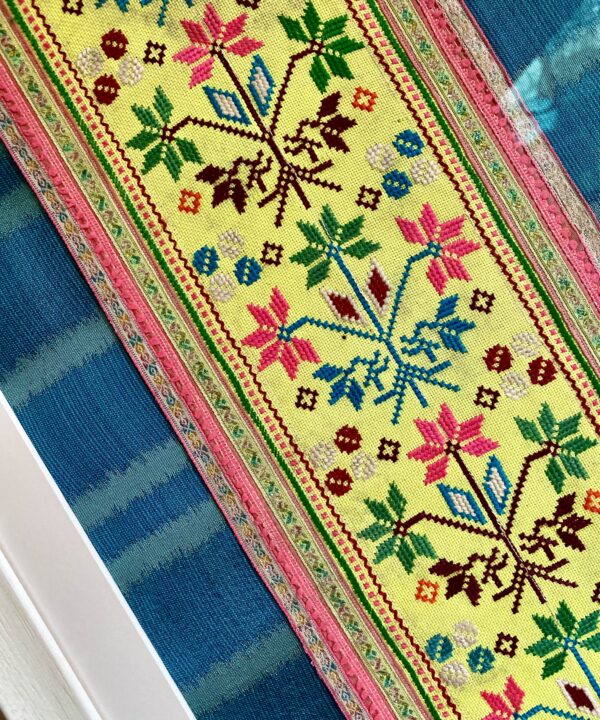 Handmade embroidery panel from Thailand framed against teal blue silk.