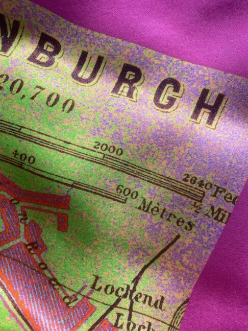 Detail of a magenta pink and lime green silk scarf depicting the city of Edinburgh.