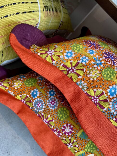 Detail of a pair of scalloped edge cushion with a colourful Aboriginal print.