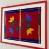 Shot from an angle a colourful, framed red art embroidery textile from Mexico.