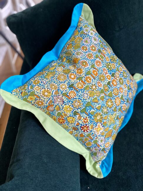Turquoise, green and yellow cushion in a cheerful Aboriginal art botanical print pattern.