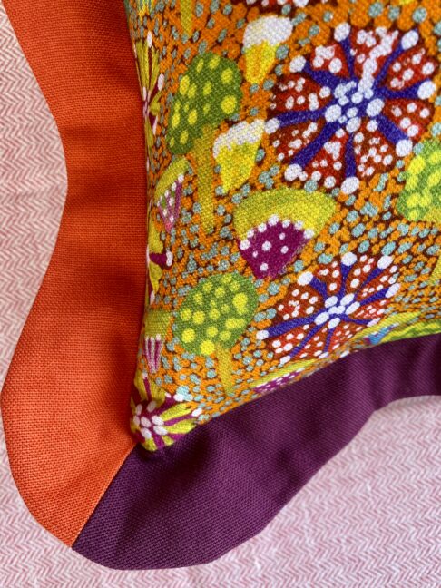 Corner detail of a colourful cushion in orange and burgundy.