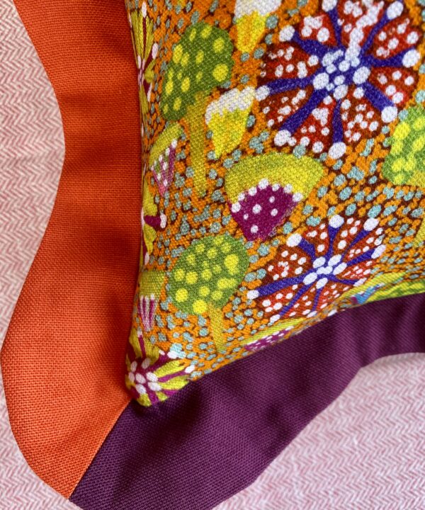 Corner detail of a colourful cushion in orange and burgundy.