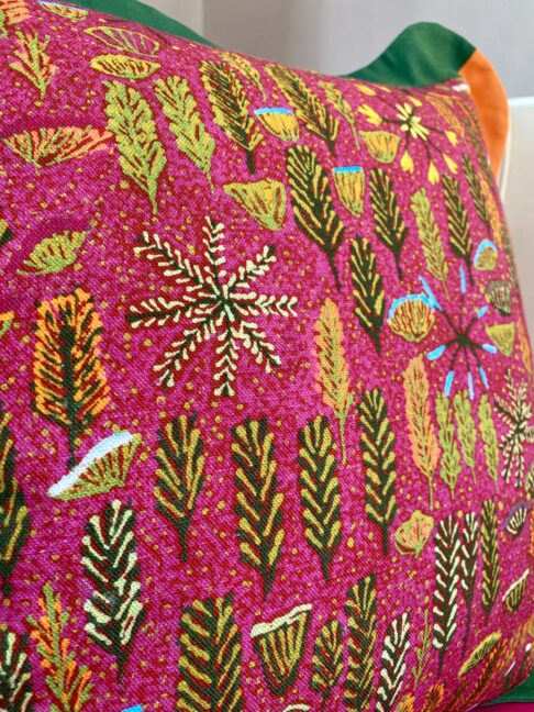 Detail of a botanical theme Aboriginal art print across a deep pink cushion.