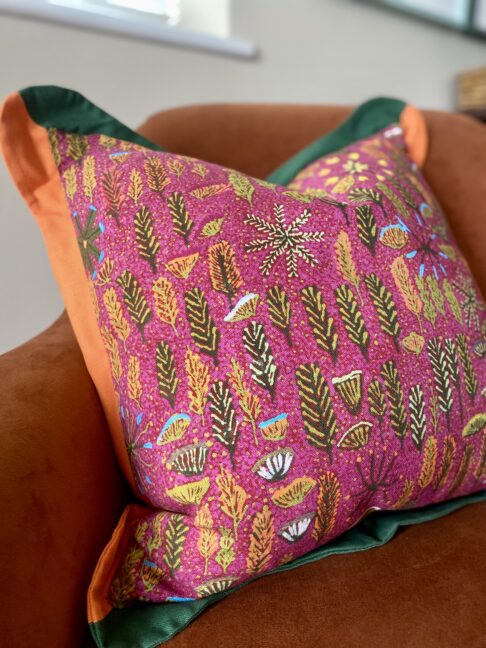 Pink indigenous Aboriginal art print on linen cushion with a scalloped green and orange Oxford trim.