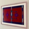 A handmade embroidery art textile in deep red and purple with a pale mauve frame and shown shot from an angle.