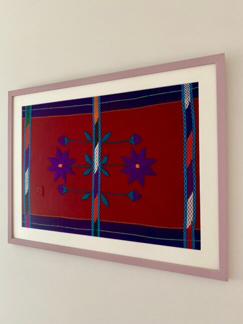 A handmade embroidery art textile in deep red and purple with a pale mauve frame and shown shot from an angle.