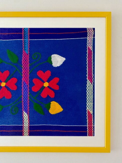 A colourful Mexican textile in blues and pinks in a bright yellow frame.