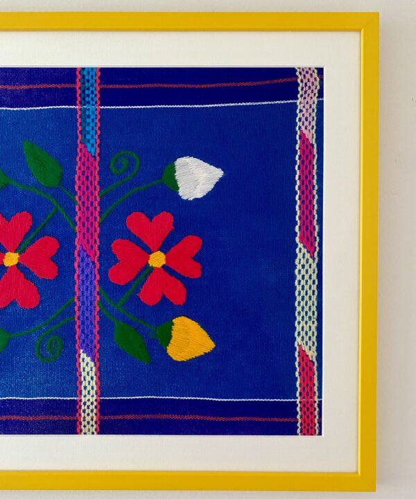 A colourful Mexican textile in blues and pinks in a bright yellow frame.