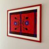 A framed floral embroidery art textile from Mexico in red and coral shown shot from the side.