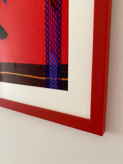 Detail of the corner of a red picture frame housing a framed Mexican textile.