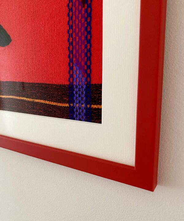 Detail of the corner of a red picture frame housing a framed Mexican textile.