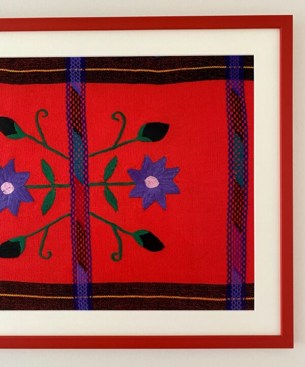 Violet embroidered flowers and buds on a bright coral ethnic Mexican cloth framed with a red picture frame.