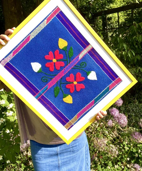 Bright yellow framed Mexican textile art depicting floral embroidery.