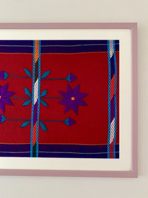 A red and purple embroidered Mexican textile framed in mauve.