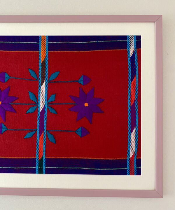 A red and purple embroidered Mexican textile framed in mauve.