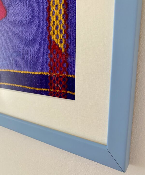 Corner detail of a pale blue frame housing a Mexican embroidery textile.