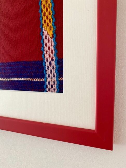 Detail of the corner of a red frame housing an embroidered Mexican textile.