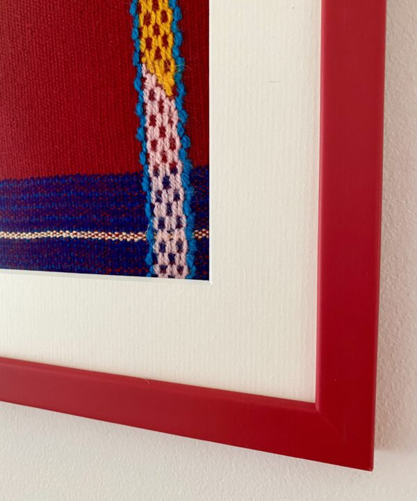 Detail of the corner of a red frame housing an embroidered Mexican textile.