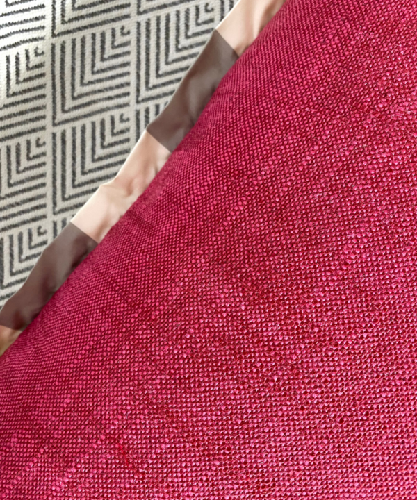 Detail of the red woven fabric reverse of a floral cushion cover with a neutral stripe trim.