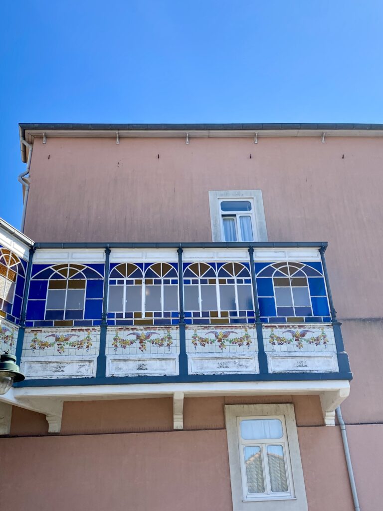 A glazed balcony in blue and orange with panels of tiled floral swags against salmon-coloured render on a building in Porto, Portugal.