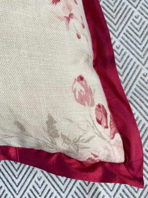 Detail of a vintage rose cushion in linen with deep red silk trim.