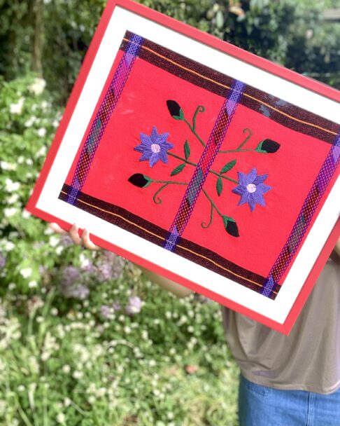 A floral embroidered textile in red and blue framed in a scarlet frame.