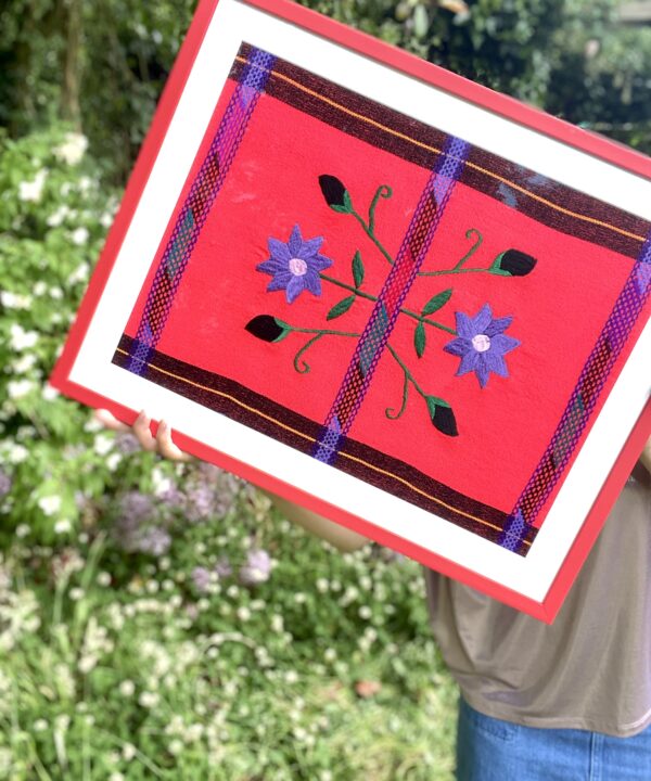 A floral embroidered textile in red and blue framed in a scarlet frame.