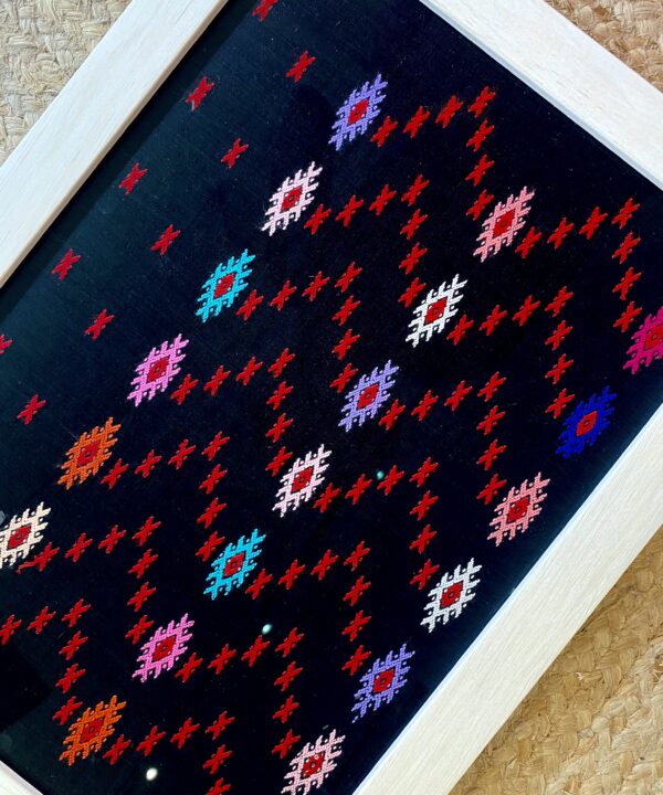 Multi-coloured stitching on a framed textile from South East Asia.