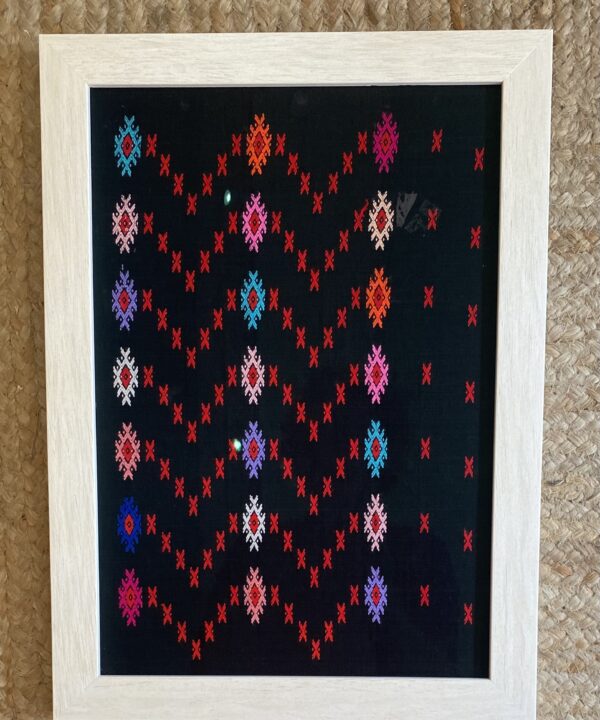 A framed textile showcasing colourful embroidery on a black cotton background, typical of South East Asian patterning.