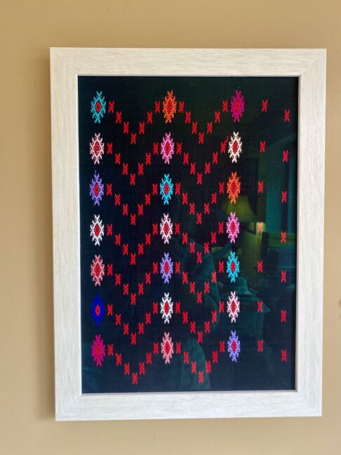 A wall art piece created from brightly coloured embroidered motifs on a black cotton ground.