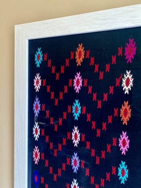 Framed textile wall art in bright coloured embroidery on a black cotton ground.