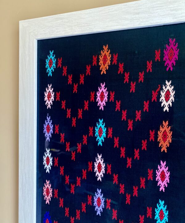 Framed textile wall art in bright coloured embroidery on a black cotton ground.