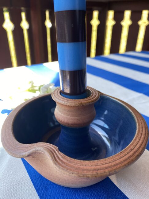 Ceramic candleholder with blue glazed interior holding a blue and brown striped dinner candle..