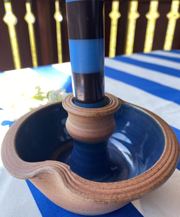 Ceramic candleholder with blue glazed interior holding a blue and brown striped dinner candle..