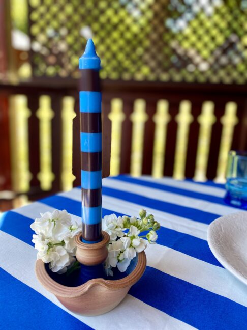 Ceramic candleholder handmade from pottery styled on a blue and white striped tablecloth with a stripy dinner candle and flowers.