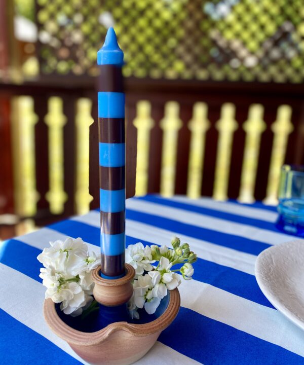 Ceramic candleholder handmade from pottery styled on a blue and white striped tablecloth with a stripy dinner candle and flowers.