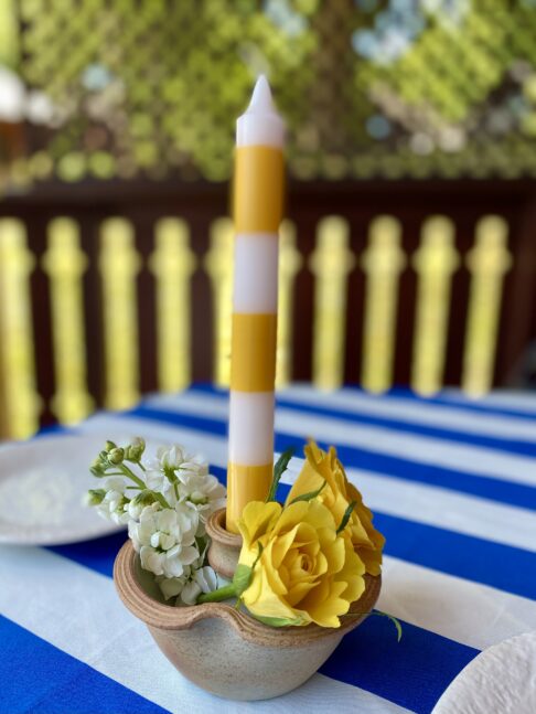 Ceramic candlestick in rustic pottery with an ivory interior glaze, yellow roses and a stripy dinner candle.