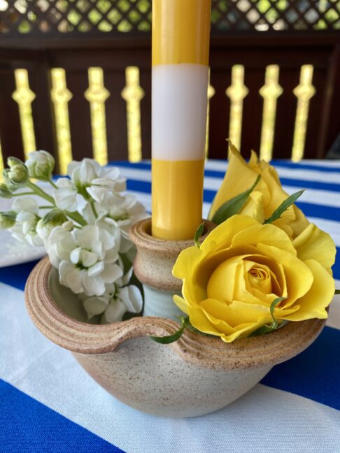 A bloom-filled ceramic candlestick with a stripy yellow and white dinner candle.