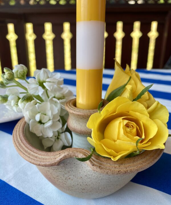 A bloom-filled ceramic candlestick with a stripy yellow and white dinner candle.