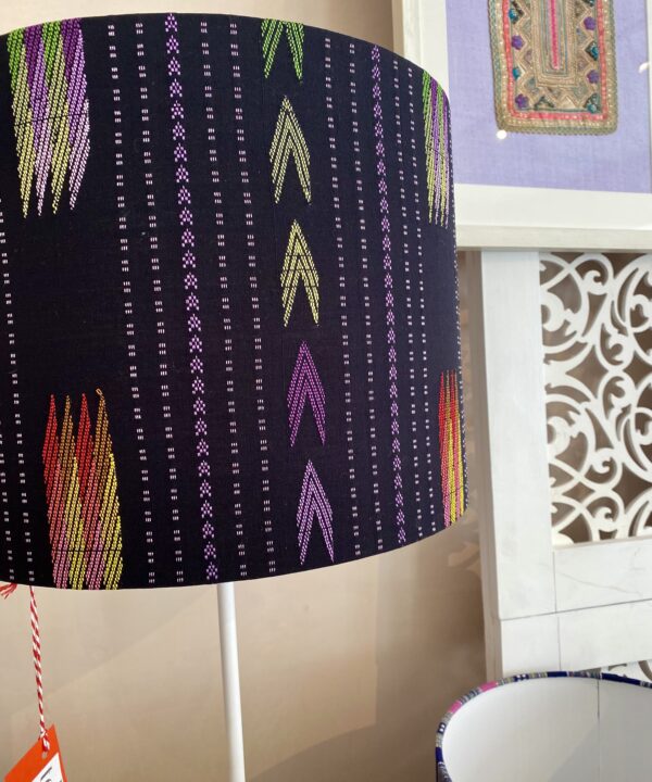 A black lampshade in a drum shape with colourful embroidered arrow detailing.