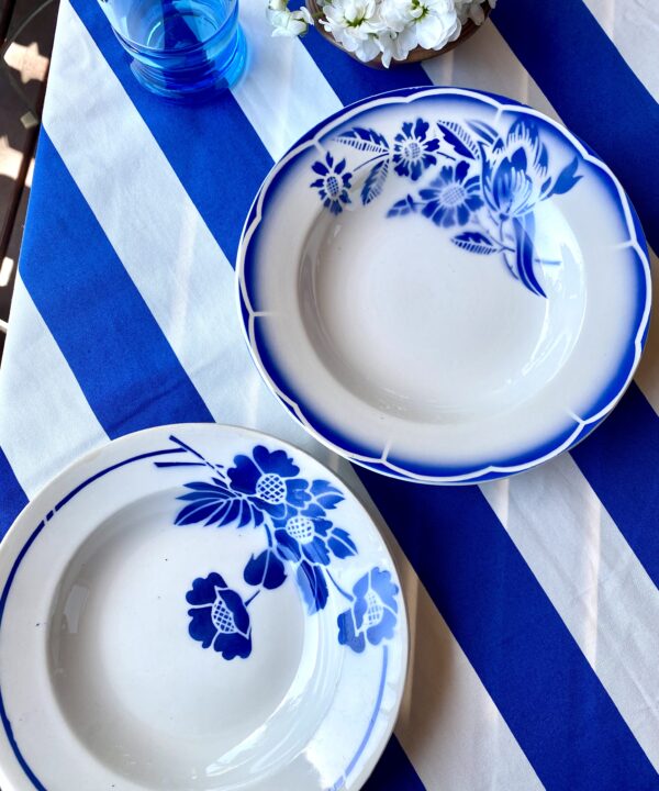 Vintage French bowls set in blue and white with transferware floral detailing shown on a Royal blue and white striped tablecloth.