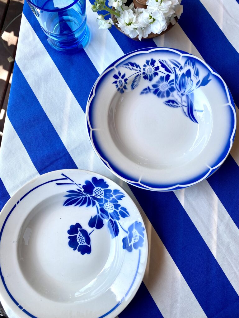 Vintage French bowls set in blue and white with transferware floral detailing shown on a Royal blue and white striped tablecloth.