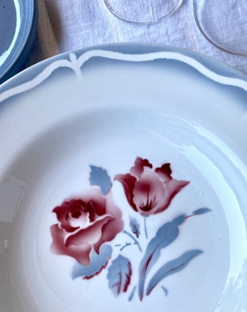 Transferware detailing on a vintage French bowl depicting scalloped edging and a rose motif in blue-grey and blush red.