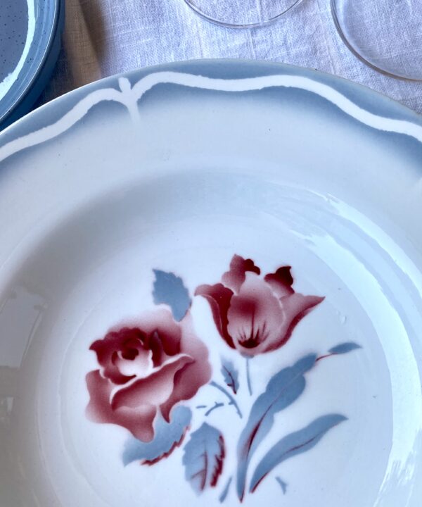 Transferware detailing on a vintage French bowl depicting scalloped edging and a rose motif in blue-grey and blush red.