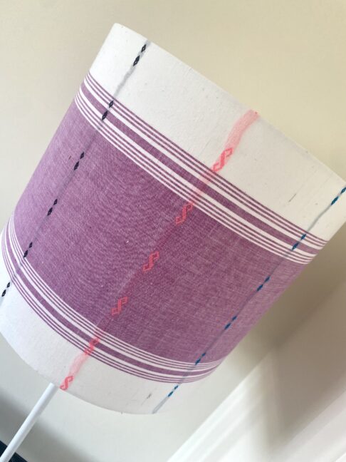 Mauve lampshades with white bands top and bottom and multi0coloured stitched detailing.