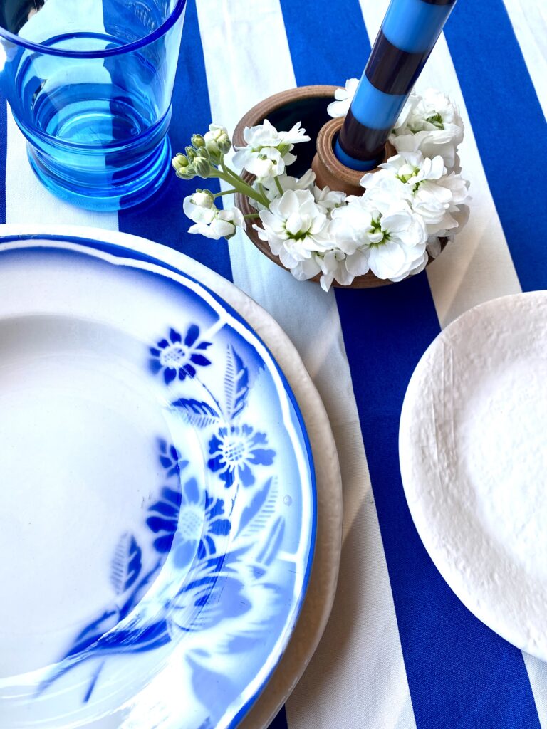 Royal blue and white place setting with striped tablecloth and vintage French blue and white bowls.